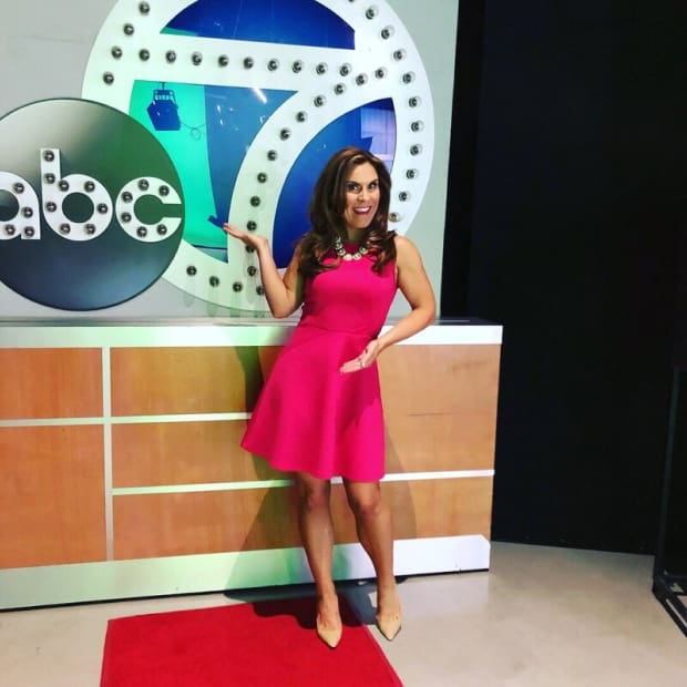 Erin King, adorned in a charming pink dress, beams with joy while situated at ABC 7 Studio exuding happiness in her expression.