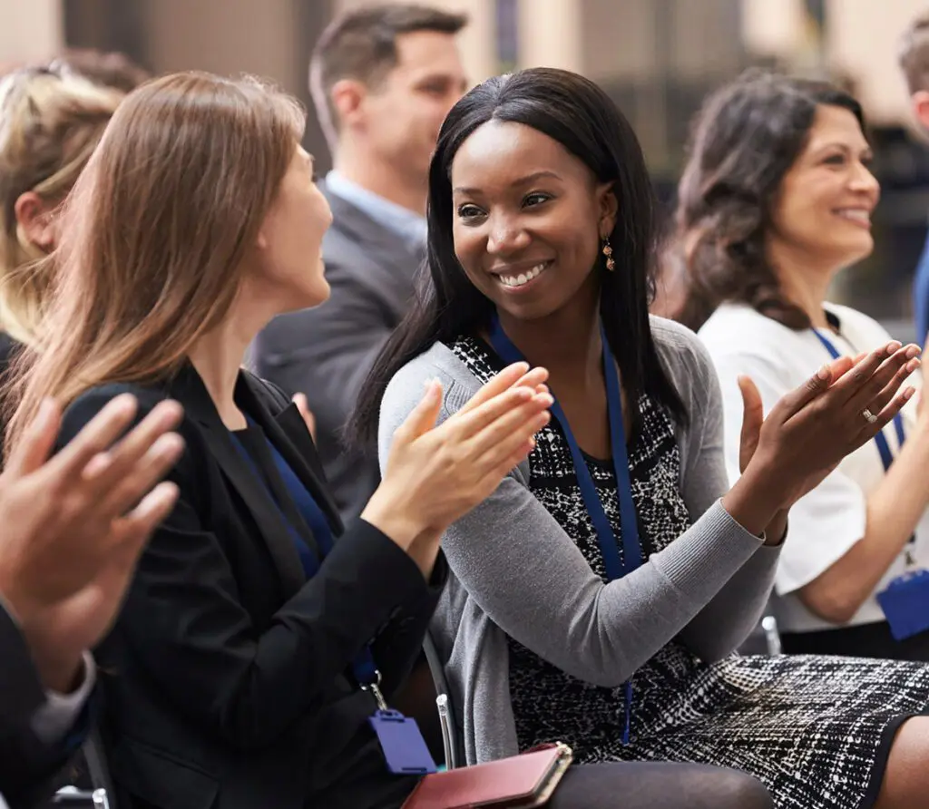 An audience captivated by Erin King's motivational speech, shown clapping enthusiastically as she delivers her empowering message at a general session.