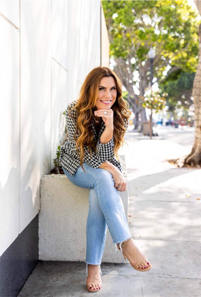 Erin King seated on a sidewalk smiling for a photo in Laguna Beach, California.